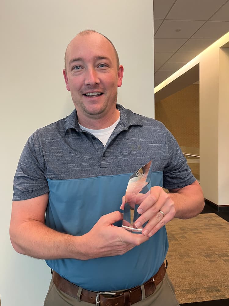 Dr. Josh Speed smiling while holding up an award.Discovery-Award